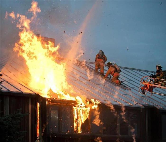 firefighters on a roof with flames billowing out of it